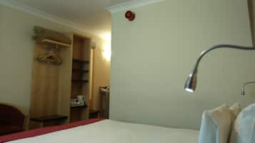 A hotel room with a bed, a wooden wardrobe, a desk, and a mirror.