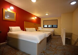 Une chambre d’hôtel avec deux lits, un grand miroir, une fenêtre avec des stores et un sol recouvert de moquette.