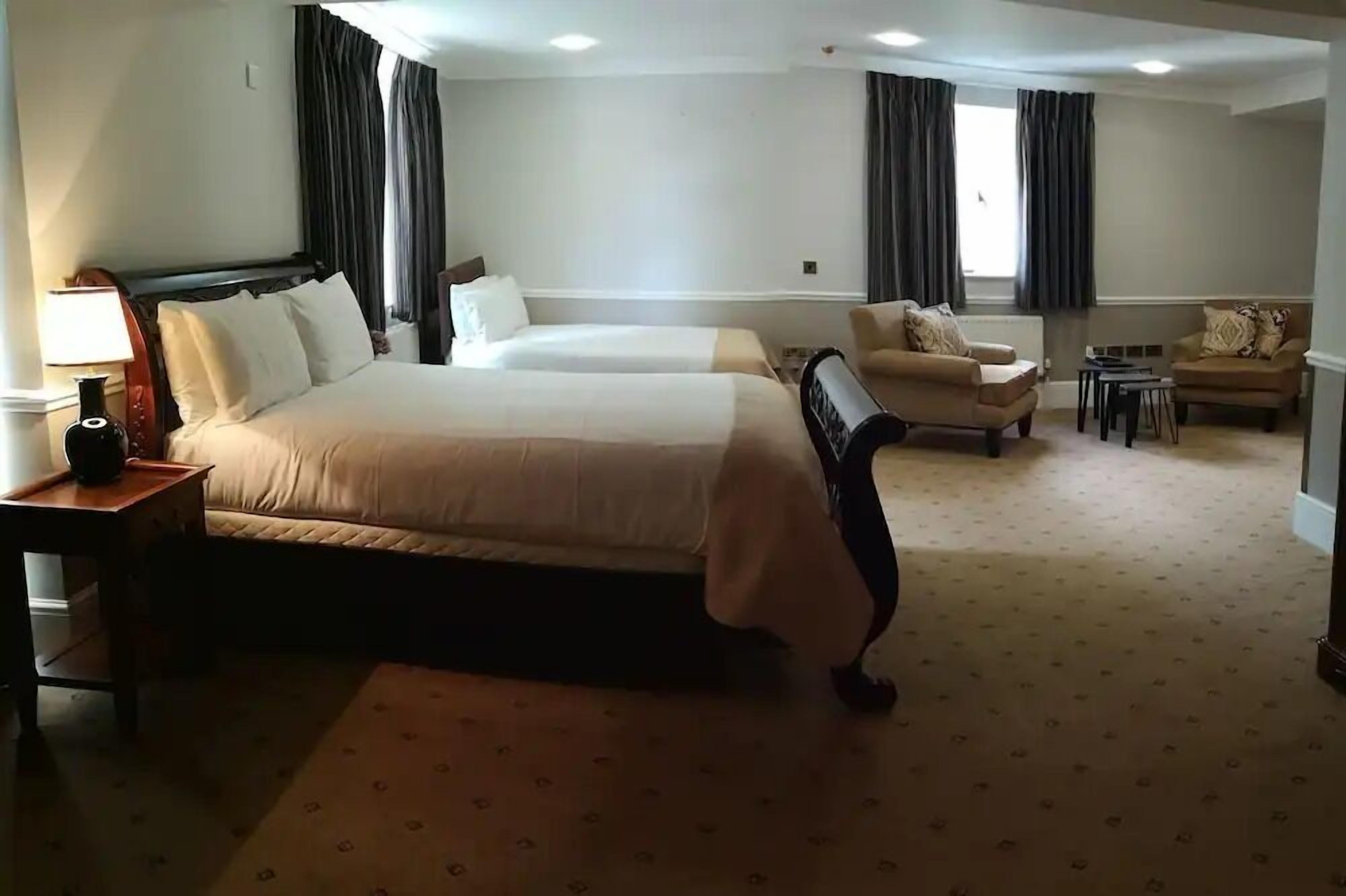 A hotel room with two beds, a sitting area with a sofa and armchairs, a small table, and a lamp.
