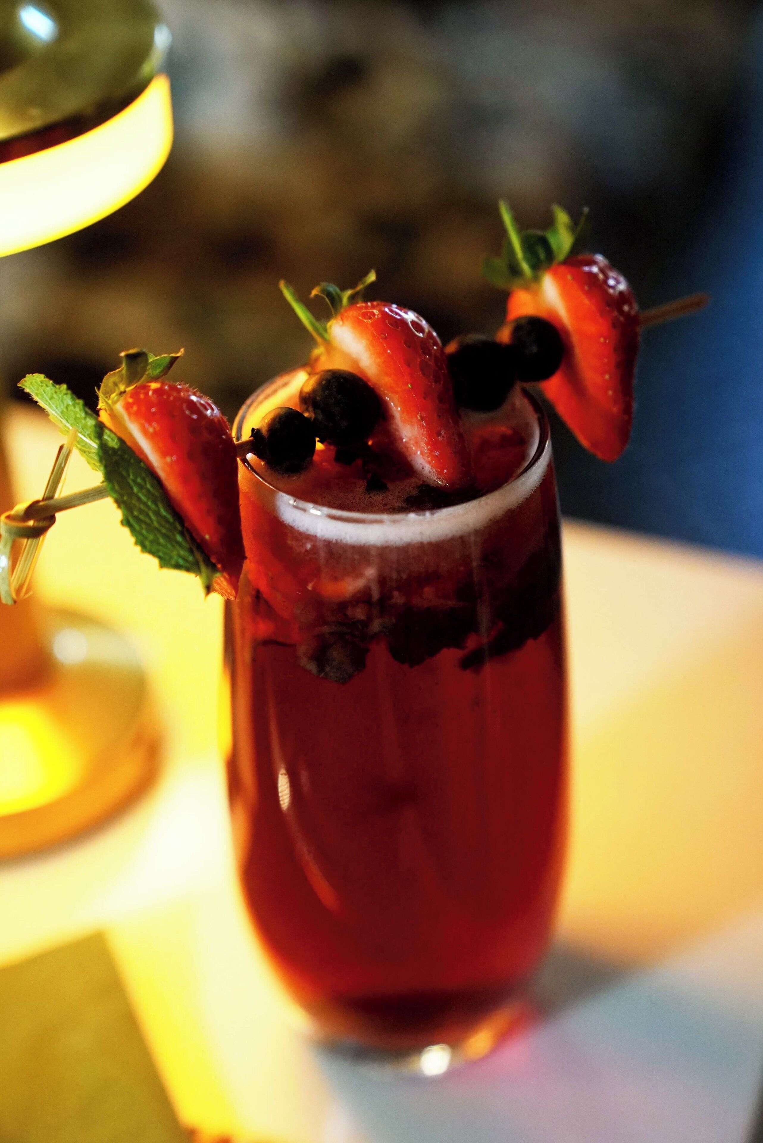 A cocktail glass with a strawberry and a mint garnish, ice cubes, and a dark liquid.