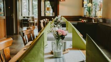 Ein Restaurantambiente mit einem für zwei Personen gedecktem Tisch, mit grünen Tischläufern, einer Blumenvase und einem Kerzenständer.