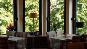 A dining area with high windows, a table, chairs, and a floor lamp. - Hotel Berghof (Nieheim)