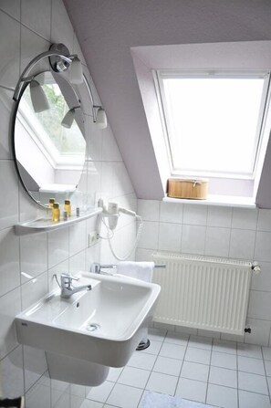 A modern bathroom with a skylight, a double sink, a mirror, and a towel rack. - Hotel Berghof (Nieheim)