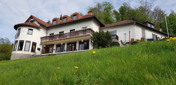 A two-story house with a balcony, a covered porch, and a sloped roof. - Hotel Berghof (Nieheim)