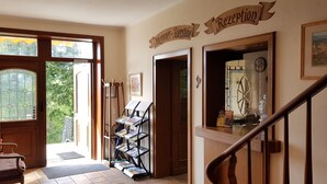 A reception area with a wooden staircase, a coat rack, and a display of magazines. - Hotel Berghof (Nieheim)