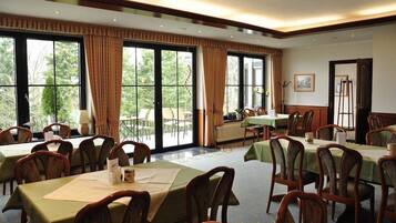 Un salón de conferencias con varias mesas y sillas, ventanas amplias con cortinas y vistas a zonas verdes.