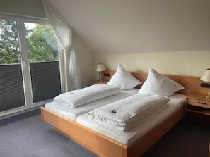 A double bed with white linens in a room with a sloped ceiling and a window with blinds. - Hotel Berghof (Nieheim)