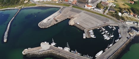 Vista aérea de un puerto con barcos amarrados, un edificio industrial grande y tierras de cultivo circundantes.