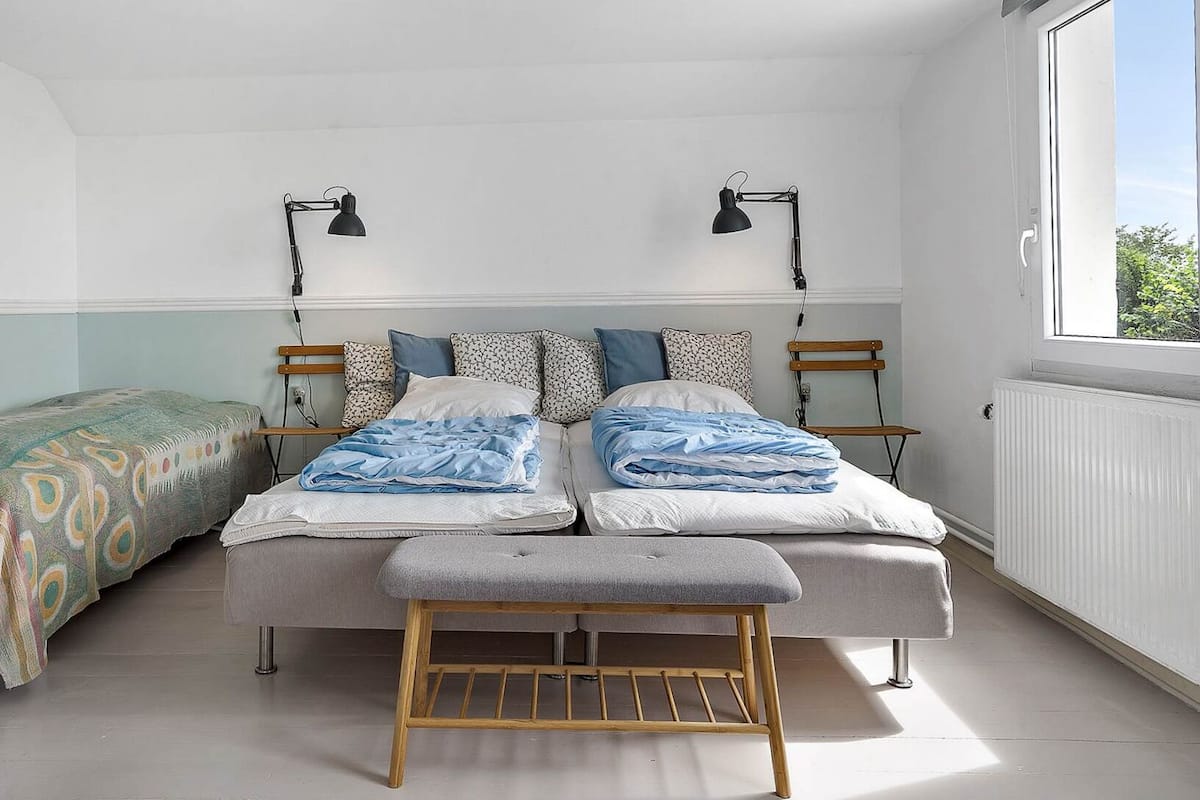 A bedroom with a bed, two bedside tables, a bench, a window, and a radiator.