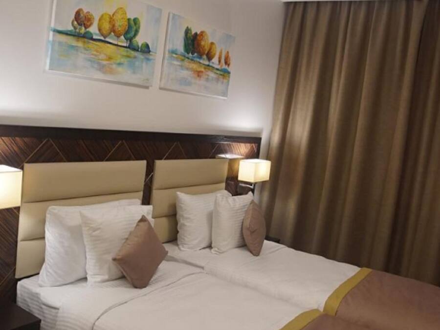 Habitación de hotel con cama, dos lámparas de pared, un control remoto y dos cuadros.