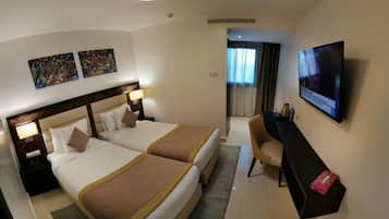 Quarto de hotel com duas camas, uma escrivaninha, televisão e obras de arte na parede.