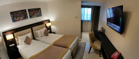A hotel room with two beds, a desk, a TV, and artwork on the wall.
