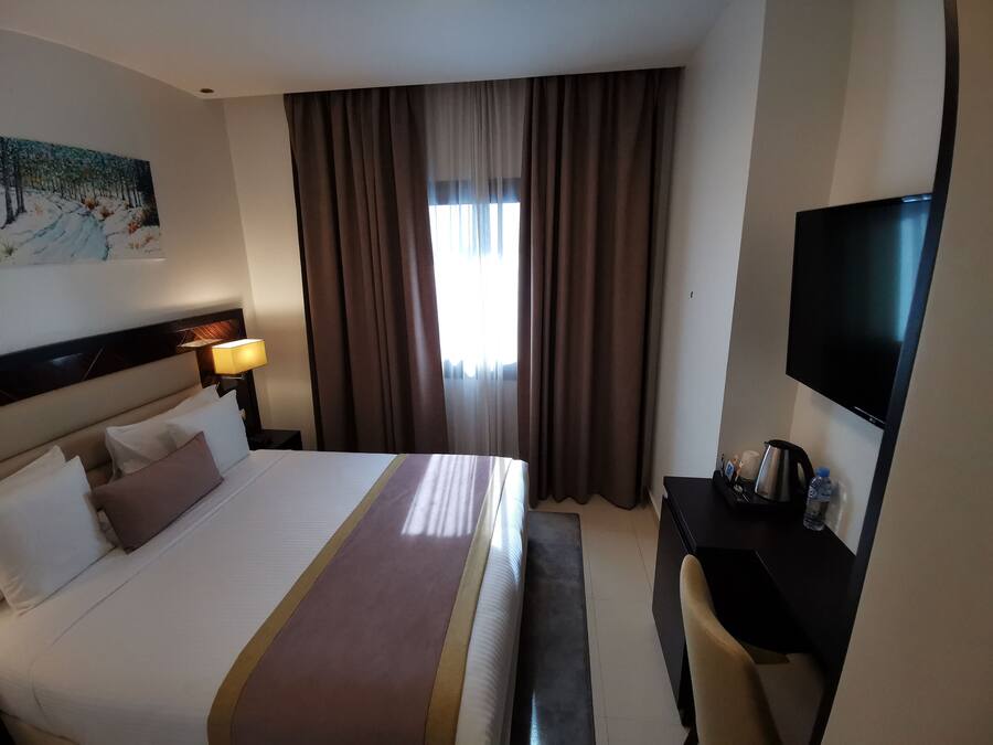 A hotel room with a bed, a TV, a desk, and a painting on the wall.
