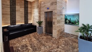 A modern lobby with a black leather sofa, a reception desk, an elevator, and a large aquarium.