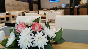 A hotel lobby with seating areas, a television screen, and a floral arrangement on a table.