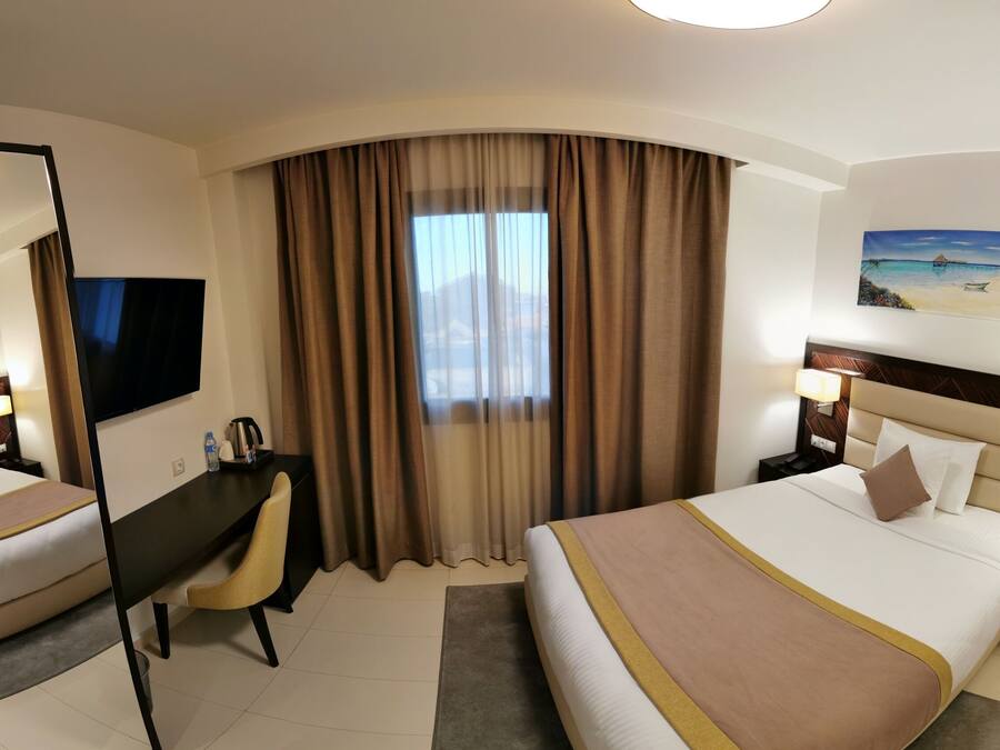 Habitación de hotel con dos camas, un escritorio, una silla, un televisor y un cuadro de una playa.