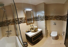 Un baño moderno con bañera, lavamanos de oro, inodoro y zona de ducha.