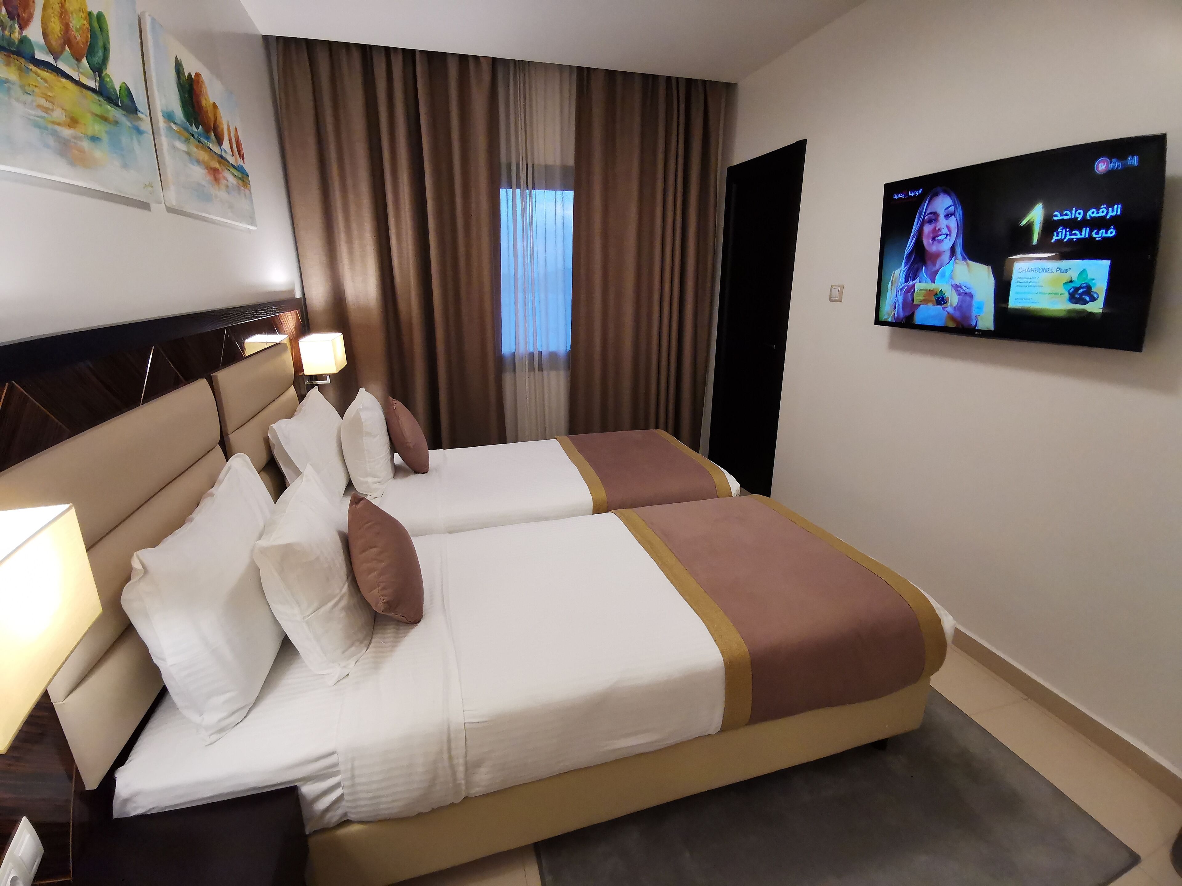 Habitación de hotel con dos camas, un televisor en la pared y una ventana con cortinas.