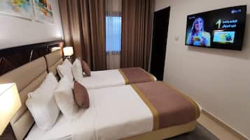 Une chambre d’hôtel avec deux lits, un téléviseur fixé au mur et une fenêtre avec des rideaux.