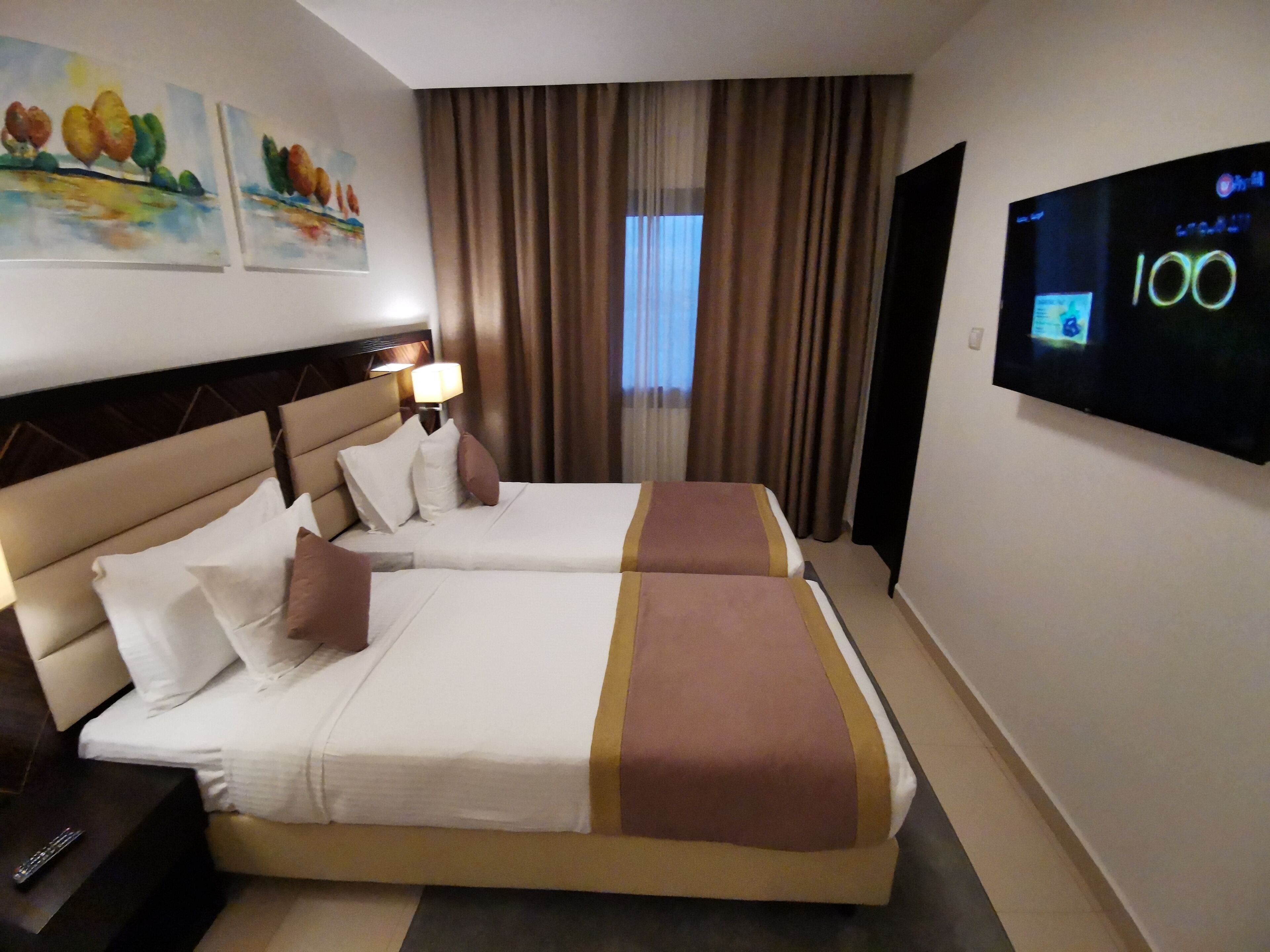 A hotel room with two beds, a TV, and artwork on the wall.
