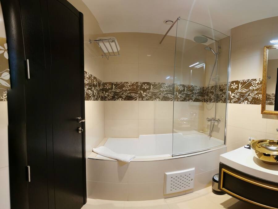 Un baño moderno con ducha envuelta en vidrio, una bañera blanca y un tocador con espejo de marco dorado.