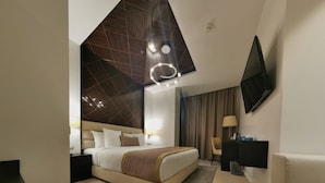 A modern hotel room with a large bed, a flat-screen TV, a desk, and a large mirror.