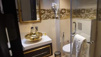 A bathroom with a gold sink, a mirror, a toilet, and a shower.