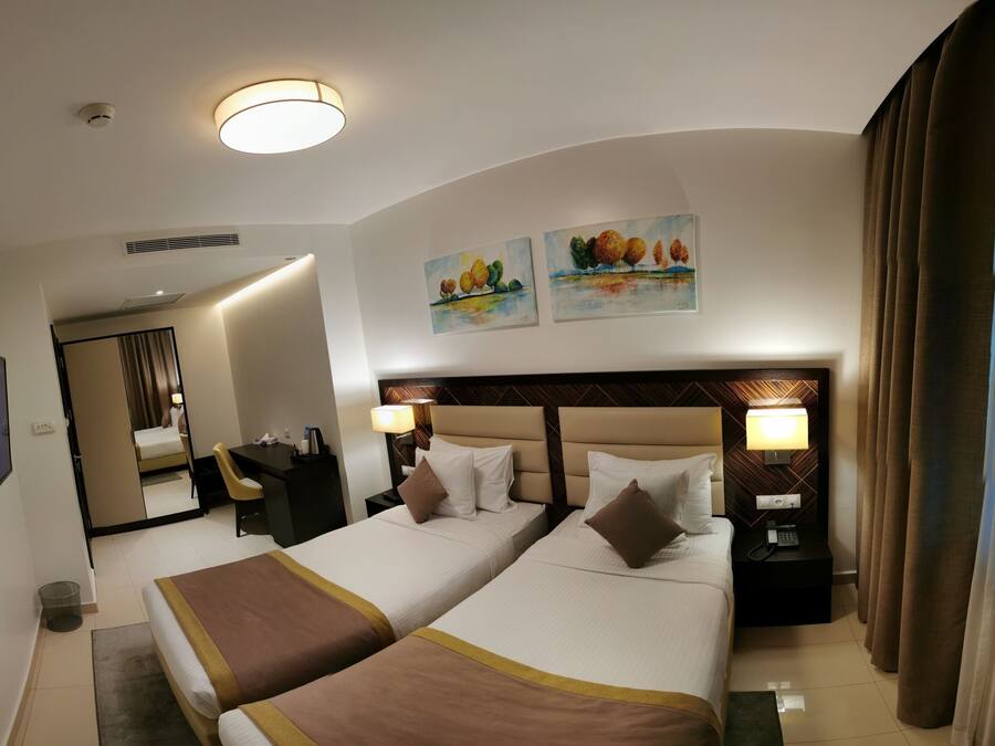 A hotel room with two beds, a desk, a chair, a TV, and artwork on the wall.