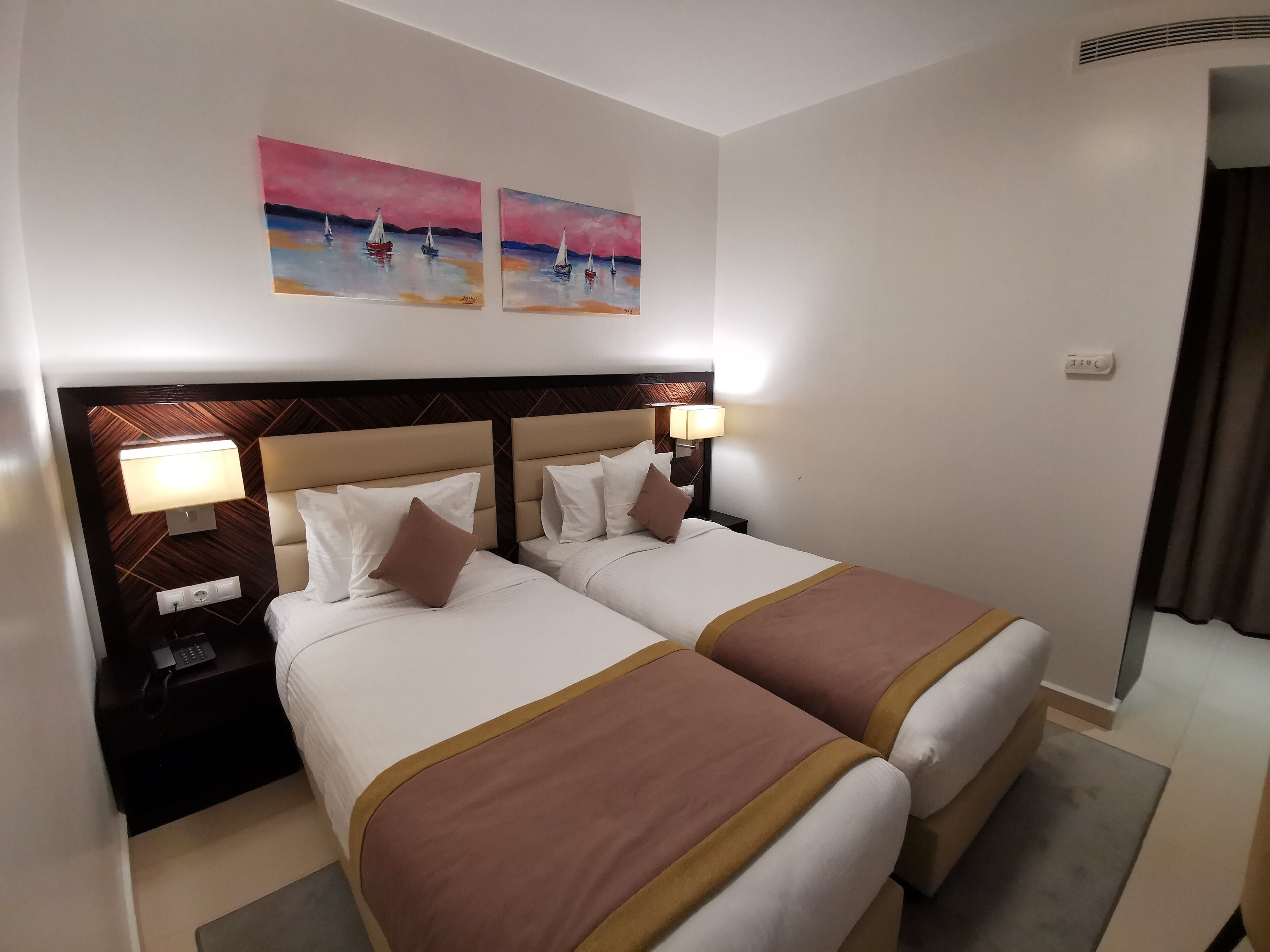 A hotel room with two beds, a nightstand with a lamp, and artwork on the wall.