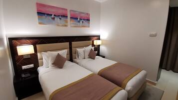 Habitación de hotel con dos camas, una mesita de noche con lámpara y una obra de arte en la pared.