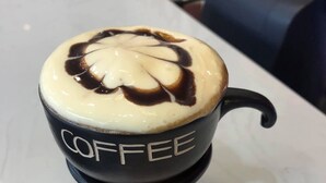 A cup of coffee with the word "COFFEE" on it, placed on a table with a candle underneath. - Hanoi Asia Hotel (Hanoi)