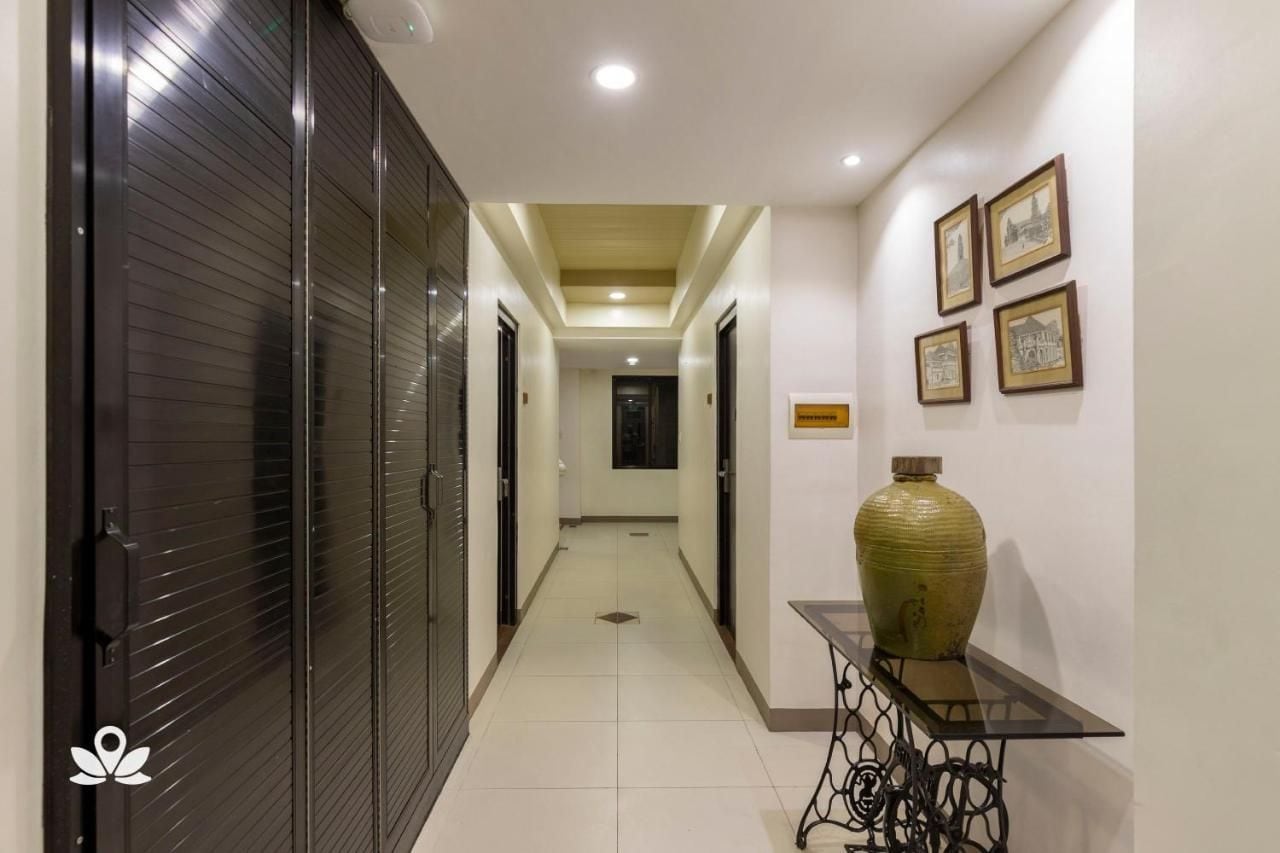 Un pasillo con puertas cerradas, una lámpara en el centro y una mesa con un florero.
