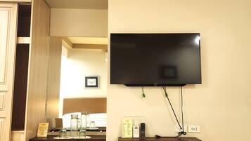 A room with a mounted TV, wooden flooring, a kitchen area with a counter, and a wooden cabinet.