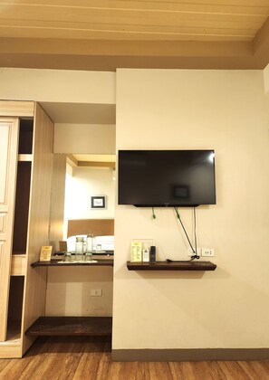 A room with a mounted TV, wooden flooring, a kitchen area with a counter, and a wooden cabinet. - Casa Marita Vigan By Zuzu (Vigan)