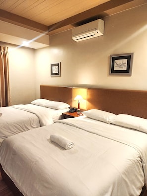 Habitación de hotel con dos camas, una mesita de noche con lámpara y un equipo de aire acondicionado en la pared.