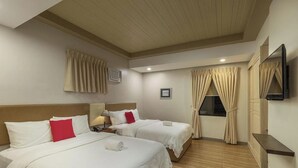 A hotel room with two beds, a TV, and a window with curtains.