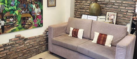 A living room with a sofa, a coffee table, a mural, and a brick wall.