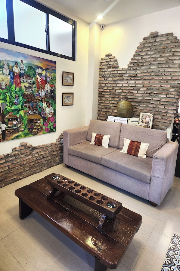 Una sala de estar con sofá, mesa de centro, un mural y pared de ladrillo.