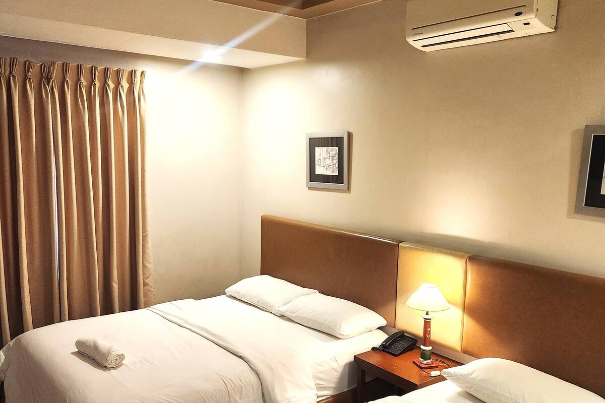 Una habitación de hotel con dos camas, una mesita de noche con lámpara, aire acondicionado y un cuadro en la pared.