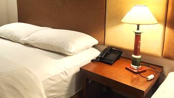 A hotel room with a bed, a bedside table with a lamp, a phone, and a framed picture on the wall.