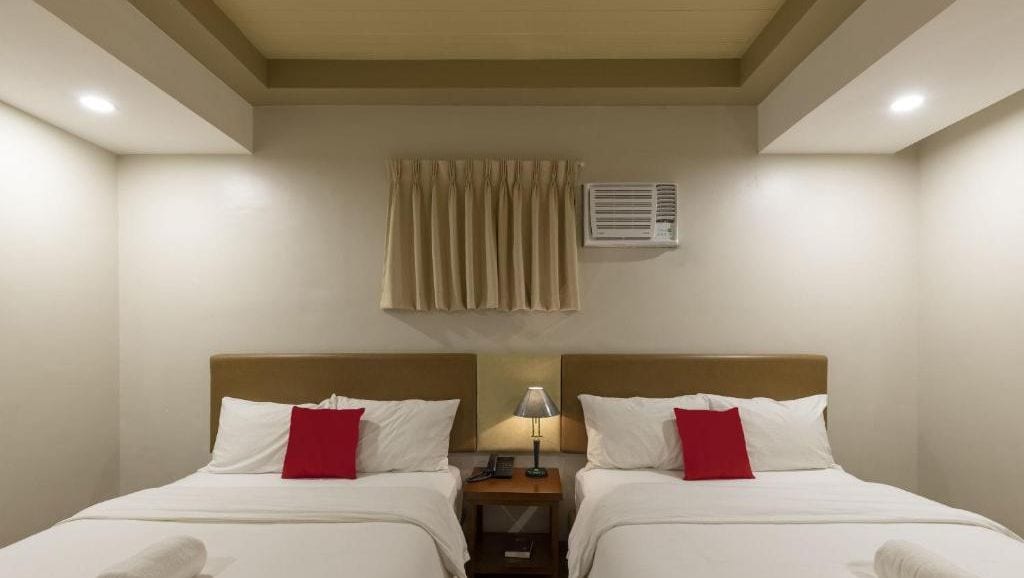 Ein Hotelzimmer mit zwei Betten, einem Nachttisch mit Lampe und einer Klimaanlage an der Wand.