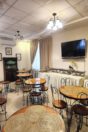 Un espace repas avec des tables rondes, des chaises, un buffet, un téléviseur et un ventilateur de plafond.