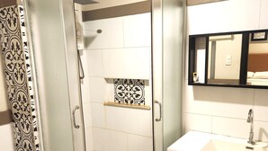 A modern bathroom with a glass-enclosed shower, a white sink, and a mirror above the sink.