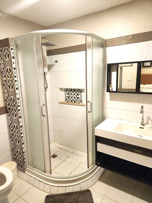 Une salle de bain moderne avec une douche à parois de verre, un lavabo blanc et un miroir au-dessus du lavabo.