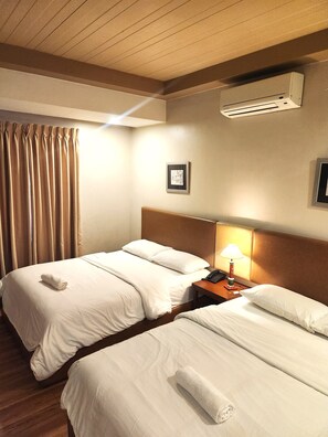 Ein Hotelzimmer mit zwei Betten, einem Nachttisch mit Lampe, einer Klimaanlage und einem gerahmten Bild an der Wand.