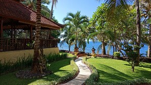 A tropical resort with a pathway leading to a building with a tiled roof, surrounded by lush greenery and palm trees. - Teluk Indah Beach & Pool Villa (Tejakula)
