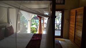 A room with a bed, a wooden door, and a view of a garden. - Teluk Indah Beach & Pool Villa (Tejakula)