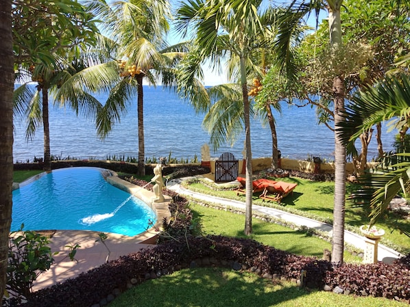 A pool surrounded by palm trees and a view of the sea. - Teluk Indah Beach & Pool Villa (Tejakula)