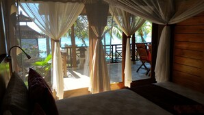 A room with a bed, a view of the sea, and a balcony with a chair and table. - Teluk Indah Beach & Pool Villa (Tejakula)