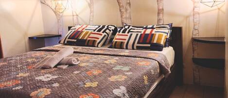 Un lit recouvert d’une courtepointe à motifs floraux, deux oreillers à motifs géométriques et une serviette enroulée.
